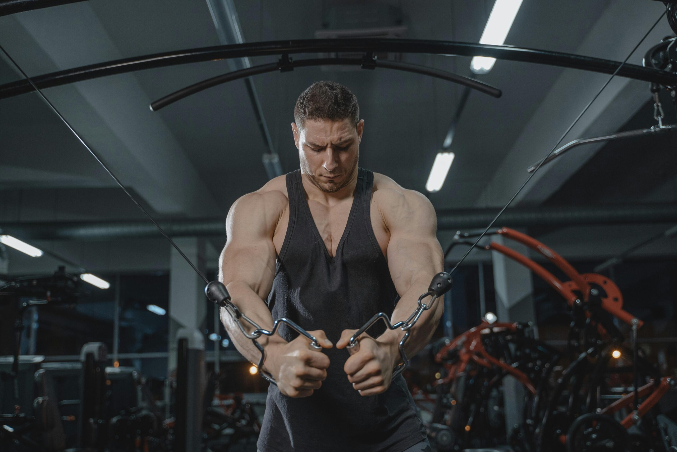 A strong man exercising on a cable crossover machine in a gym setting.