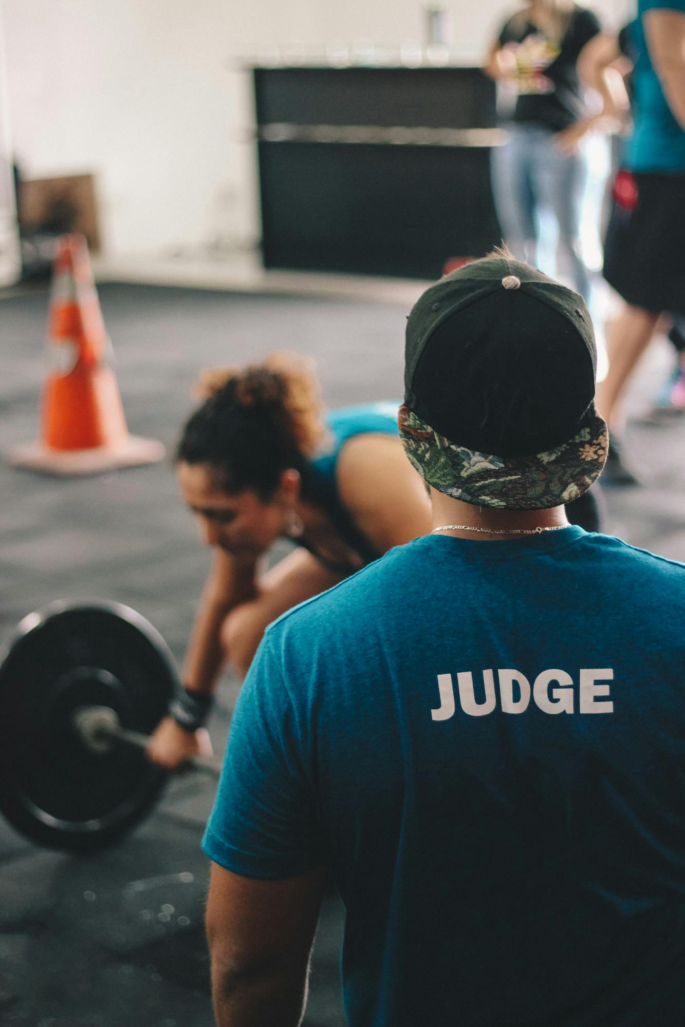 A CrossFit judge keeps an eye on a female athlete during a weightlifting event indoors.